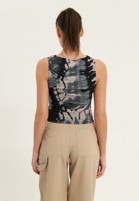Top sin mangas de teñido anudado en negro y gris con un diseño ajustado, que presenta un escote redondeado y una textura fruncida, combinado con pantalones de pierna ancha en beige.