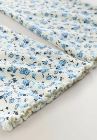 Tela acanalada floral en amarillo pálido, con pequeñas flores azules y negras. Los bordes tienen un ribete fruncido para un detalle adicional.