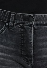 Pantalones vaqueros de mezclilla negra con un acabado desgastado, que cuentan con un botón de metal, trabillas para el cinturón y un detalle de costura en contraste a lo largo de la costura lateral.