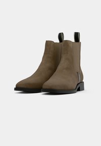 Bottines en suede marron avec un bout arrondi, des panneaux élastiques sur les côtés, une languette de tirage et un petit talon bloc. Semelle en caoutchouc noir pour une meilleure adhérence.