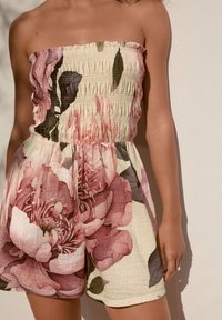 Combinaison-short florale avec un design bustier et un corsage smocké. Confectionnée dans un tissu léger aux teintes roses douces et vertes.