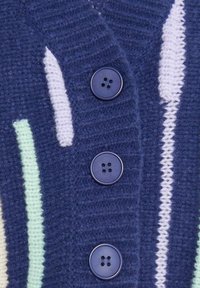 Jūras spēku vilnas kardigāns ar vertikālām svītrām baltā, gaiši zaļā un lavandas krāsā; ar trim tumšiem pogām, katra ar četriem caurumiem.