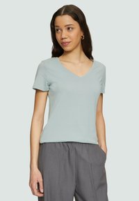 Hellblaues T-Shirt mit kurzem Arm und V-Ausschnitt aus weichem Stoff, kombiniert mit grauen, taillierten Hosen. Es zeichnet sich durch einen lockeren Schnitt und eine glatte Textur aus.