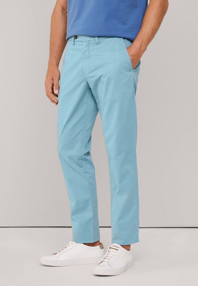 Pantalones de color azul claro con una textura suave, diseño de pierna recta, con trabillas para el cinturón, bolsillos frontales y cierre con botón. Combinados con zapatillas blancas.