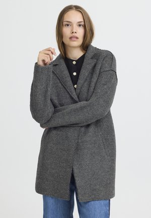 Manteau en laine gris avec un col à revers, finition texturée, poches avant et coupe droite, associé à un haut noir et un jean bleu.