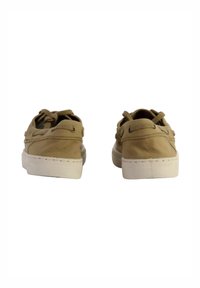 Zapatos de lona color beige con suelas de goma blanca, que presentan un diseño de cordones y ojales, mostrando una textura suave y una forma redondeada.