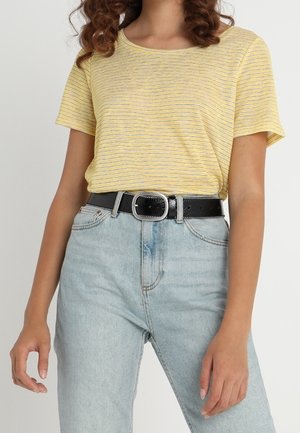 Femme portant un t-shirt rayé jaune à manches courtes, rentré dans un jean bleu clair taille haute avec une ceinture noire et une boucle argentée.