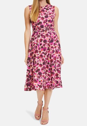 Vestito rosa senza maniche con motivi circolari rossi e viola, lunghezza al ginocchio, abbinato a sandali rosa con tacco alto e cinturino alla caviglia indossati da una donna.
