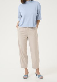 Ljusblå kortärmad topp med hög halsringning; beige högmidjade, lösa byxor; ljusblå fransförsedda klacksandaler.