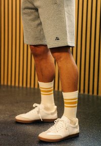 Grå sportshorts med en svart logotyp, matchat med vita strumpor med två gula ränder och vita sneakers med en brun sula.