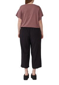 Lockere, kurzärmelige Bluse in Mauve mit Rundhalsausschnitt, kombiniert mit schwarzen, weit geschnittenen Hosen. Die Schuhe verfügen über dicke Plateausohlen.