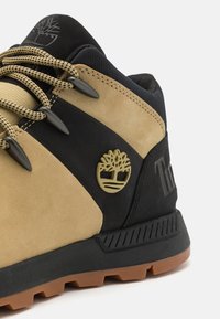Stivali da trekking marroni e neri realizzati in materiali scamosciati e in gomma. Presentano un logo impresso, dettagli testurizzati e colori delle stringhe a contrasto.