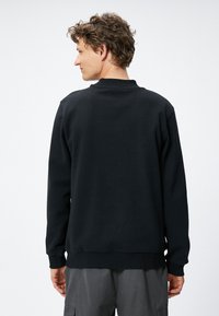 Czarny sweatshirt z okrągłym dekoltem i ściągaczami, charakteryzujący się prostym wzornictwem i miękką teksturą, widziany z tyłu.
