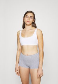 White sports bra with wide straps, paired with light grey boyshorts, displayed against a neutral background. Minimalistic design, soft fabric texture.