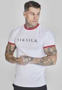 Witte t-shirt met korte mouwen, voorzien van een rode kraag en mouwen; heeft een zwart "SIKSILK" logo op de voorkant. Het materiaal lijkt glad en aansluitend.