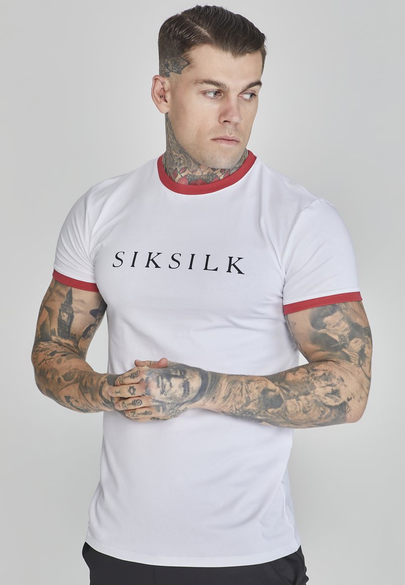 Witte t-shirt met korte mouwen, voorzien van een rode kraag en mouwen; heeft een zwart "SIKSILK" logo op de voorkant. Het materiaal lijkt glad en aansluitend.