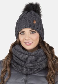 Căciulă tricotată gri cu un model texturat și pom-pom negru, asociată cu o eșarfă infinite gri, evidențiind un material moale și confortabil.