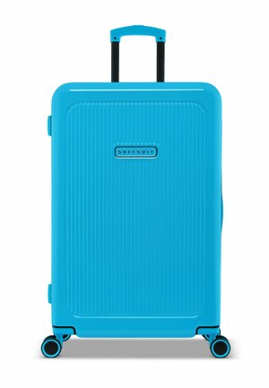 Light blue hard-shell suitcase with vertical ribbed texture, a retractable handle, and four multi-directional wheels. Brand logo displayed.