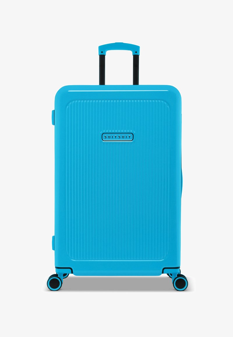 Lichtblauwe harde koffer met verticale ribbeltextuur, een uitschuifbare handgreep en vier multi-directionele wielen. Merkenlogo zichtbaar.