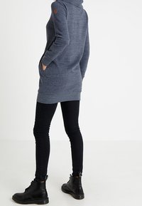 Abito felpato grigio con maniche lunghe, tasche laterali e cappuccio. Indossato con jeans skinny neri e stivali neri con lacci. Logo in pelle sul braccio.