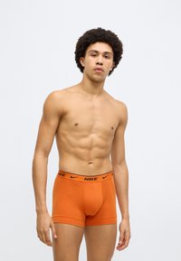 Πορτοκαλί βαμβακερά μπόξερ με μαύρο λογότυπο Nike στη ζώνη μέσης, με εφαρμοστή σχεδίαση και λεία υφή.