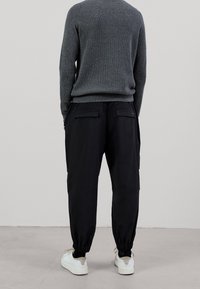 Pantaloni cargo neri con polsini elasticizzati, dotati di due tasche posteriori, indossati con un maglione grigio scuro strutturato e sneakers bianche.
