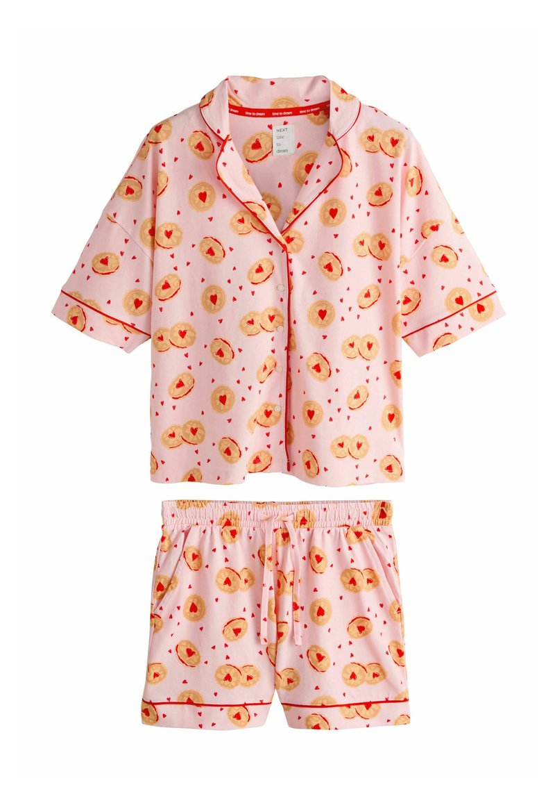 Set roz de pijama, format dintr-un top cu nasturi cu mâneci scurte și pantaloni scurți asortați. Materialul are un model cu fursecuri decorate cu inimioare și accente roșii.