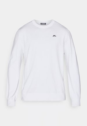 Bílý dlouhý svetr vyrobený z bavlny, s kulatým výstřihem, vroubkovanými manžetami a malým černým logem na levé části hrudi.