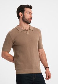Polo de manga corta en marrón claro, de tela texturizada con un collar clásico y una tapeta de tres botones. Puños y dobladillo acanalados.