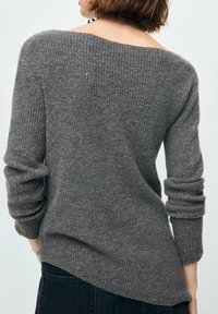 Suéter gris de punto acanalado con un escote profundo en la espalda, mangas ajustadas y un dobladillo ligeramente más largo en la parte posterior. Textura suave con un ajuste relajado.