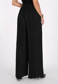 Wide-leg black pleated pants with a high waistband and a textured fabric, featuring a smooth finish and subtle vertical lines.