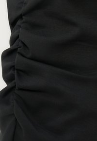 Tissu noir avec texture froncée et plissée créant des plis horizontaux et des ombres douces sur un fond clair.