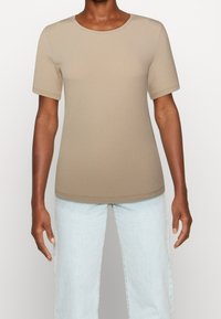 T-shirt beige a maniche corte con colletto rotondo. Tessuto morbido, design leggermente aderente. Abbinato a jeans in denim blu chiaro.