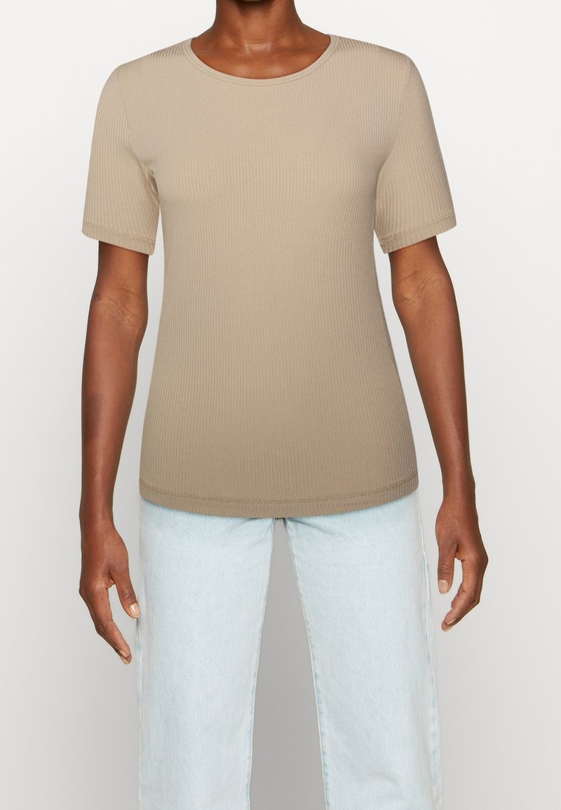 T-shirt beige a maniche corte con colletto rotondo. Tessuto morbido, design leggermente aderente. Abbinato a jeans in denim blu chiaro.
