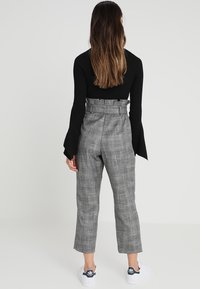 Pantaloni a vita alta e gamba larga in un motivo a quadri grigi, con un tessuto testurizzato e dettaglio con cintura, abbinati a sneakers bianche.