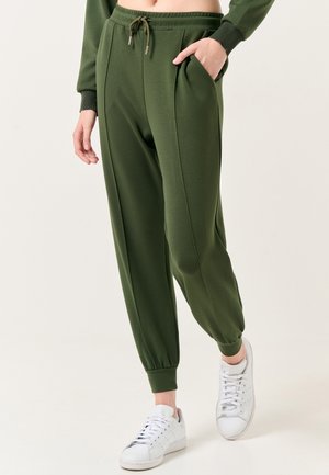 Pantaloni jogger verdi, sfumati e con vita regolabile, tasche laterali e caviglie affusolate abbinati a sneakers bianche. Tessuto morbido e liscio.