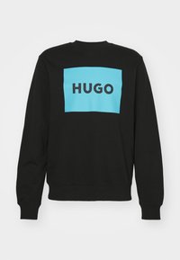 Svart sweatshirt med en stor ljusblå rektangulär grafik med ordet "HUGO" i fet svarta bokstäver. Rundad halsringning och långa ärmar.