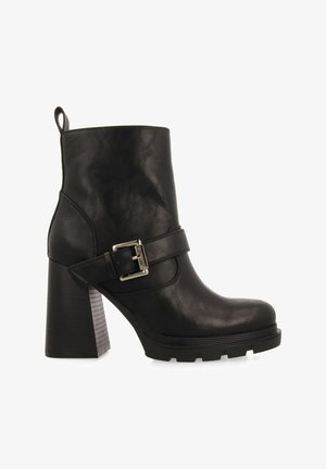 Botín negro de cuero hasta el tobillo con un grueso tacón cuadrado, que presenta una correa lateral y un acento de hebilla plateada. Suela texturizada para mayor agarre.