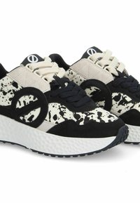 Des sneakers noir et blanc avec une surface texturée, arbore un motif tacheté, un accent circulaire proéminent et des lacets couleur crème.