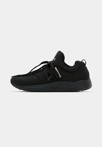 Black athletic shoes with a mesh and synthetic upper, featuring a sleek design, padded collar, and textured sole. Accented with subtle hardware.