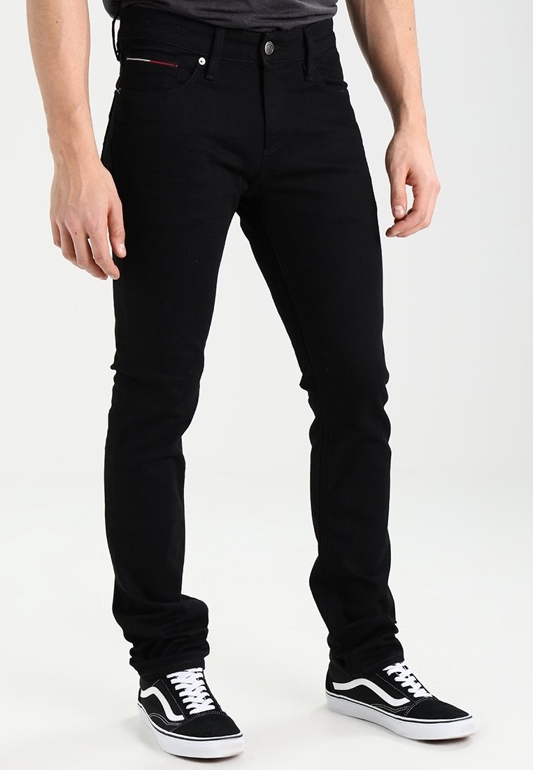 Svart slim-fit jeans med femfickorsdesign, knappstängning och subtila röda sömmar på bakfickan; används med svarta sneakers.