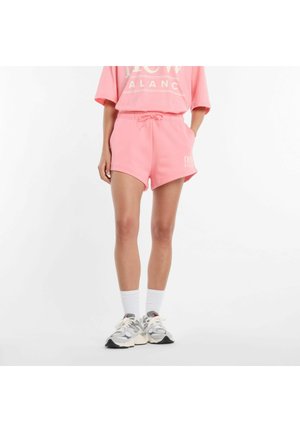 Person trägt pinke Shorts und passendes übergroßes T-Shirt, weiße Socken und graue klobige Sneaker, steht vor weißem Hintergrund.
