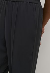 Pantalons sombres et amples en tissu lisse avec une taille élastique. Comprend des poches latérales et de délicats plis.