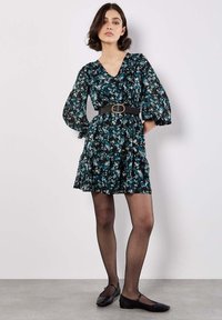 Robe noire à motifs floraux bleus et verts, décolleté en V, manches bouffantes, cintrée à la taille par une ceinture noire, jupe évasée, associée à des ballerines noires.