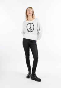 Suda gris claro con mangas oversized y símbolo de paz negro, combinado con pantalones slim de piel sintética negra y botas negras gruesas.