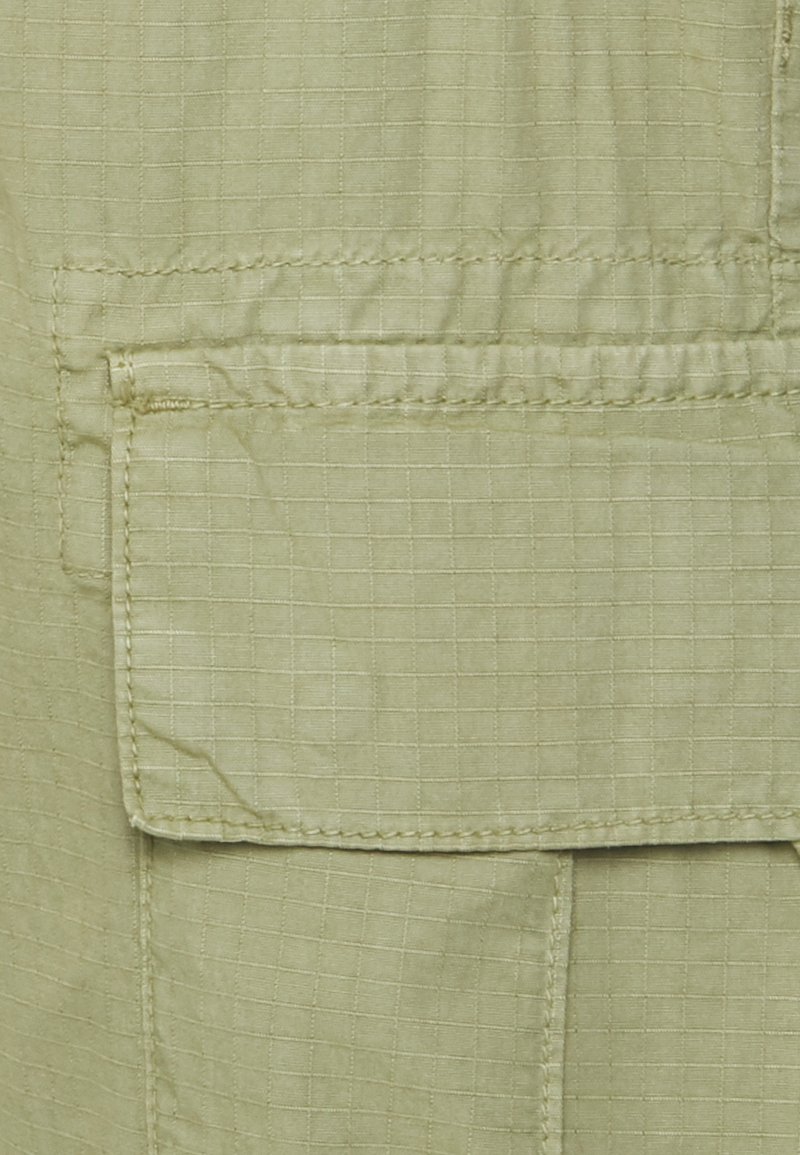 Jasnozielony materiał w kratkę, z przednią kieszenią z klapką i przeszyciami. Gładka tekstura i kompaktowy design.