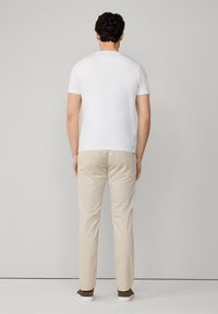 T-shirt bianca a maniche corte abbinata a pantaloni beige chiaro. Il modello è di spalle, mettendo in evidenza un design semplice e una forma aderente.