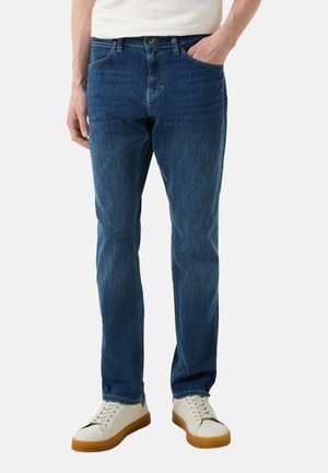 Dunkelblaue Jeans aus Denim mit geradem Schnitt, fünf Taschen und Reißverschluss. Kombiniert mit cremefarbenen Sneakers mit einer braunen Sohle.