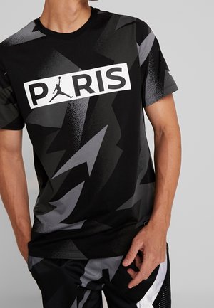 T-shirt noir avec un motif d'éclairs gris, un logo "PARIS" blanc et un graphisme Jumpman. Manches courtes ; tissu doux.