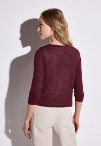 Burgundy långa ärmar topp gjord av lätt tyg, med rundad halsringning och åtsittande ärmar, parat med ljusbeige byxor.